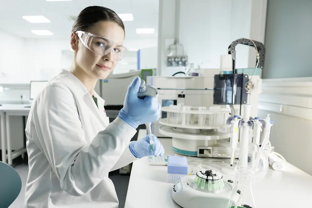 Una científica experimenta en un laboratorio, con bata y gafas de seguridad.