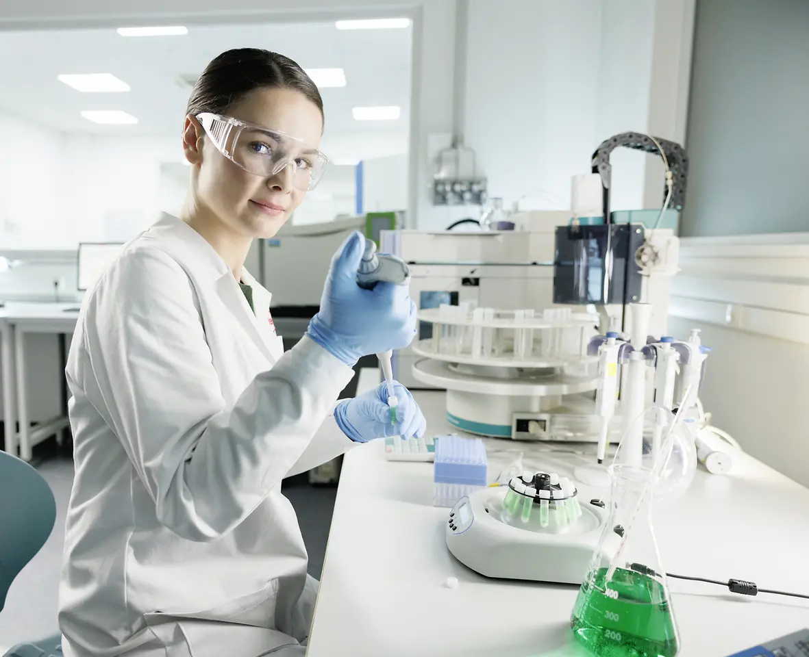 Una científica experimenta en un laboratorio, con bata y gafas de seguridad.