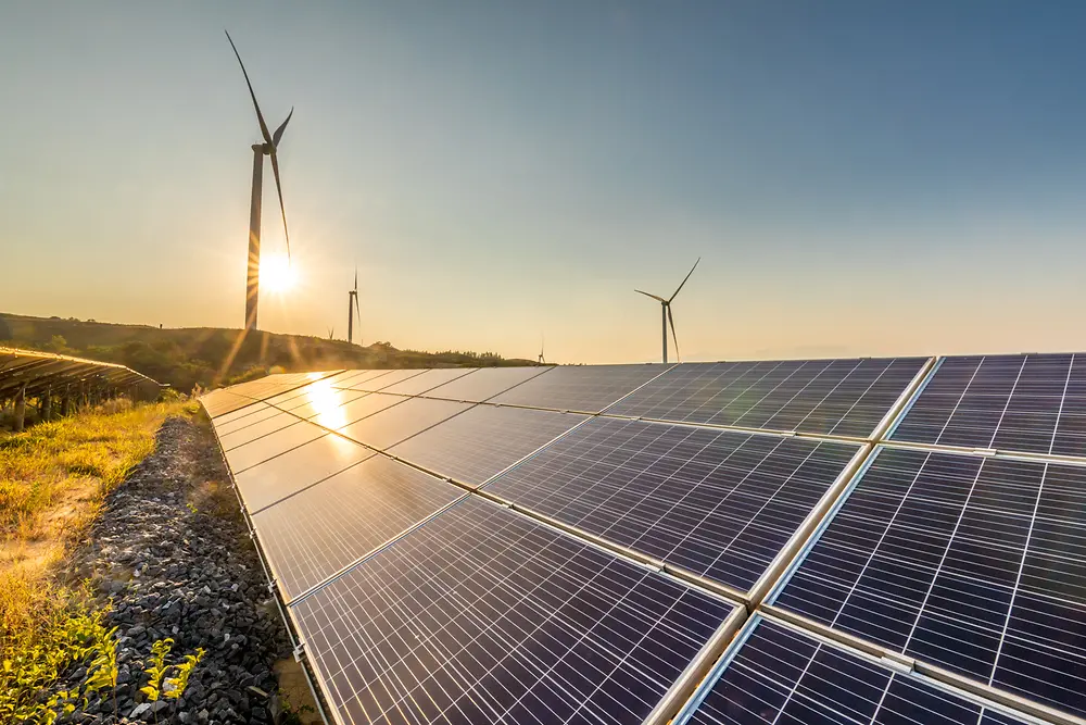 Paneles solares al atardecer con molinos de viento en el fondo.