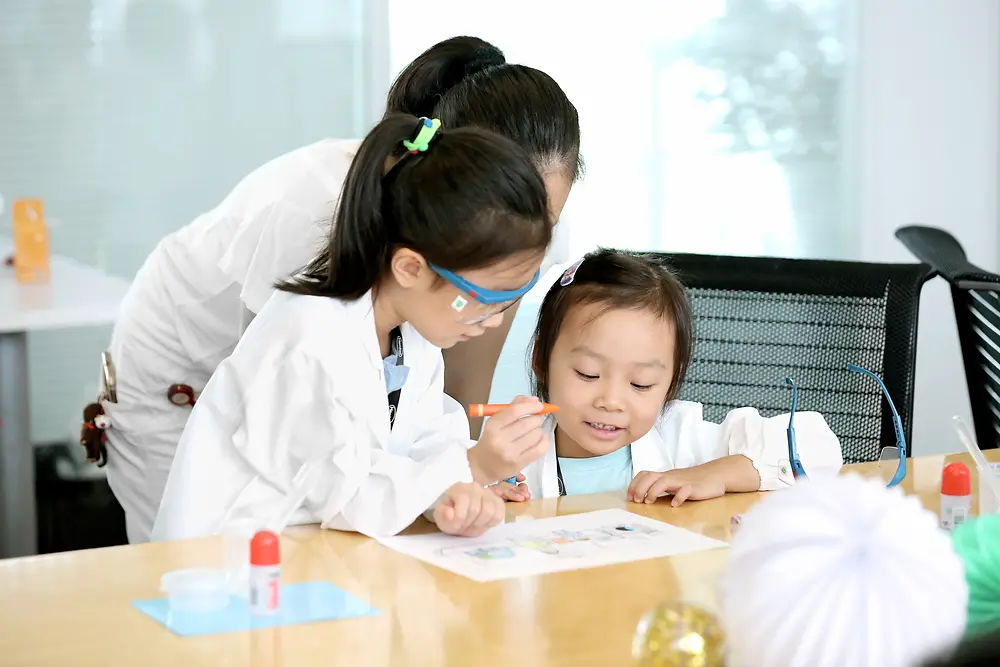 Dos niños y una señora con batas de laboratorio.