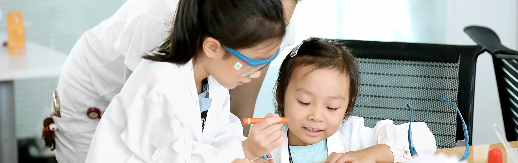 Dos niños y una señora con batas de laboratorio.